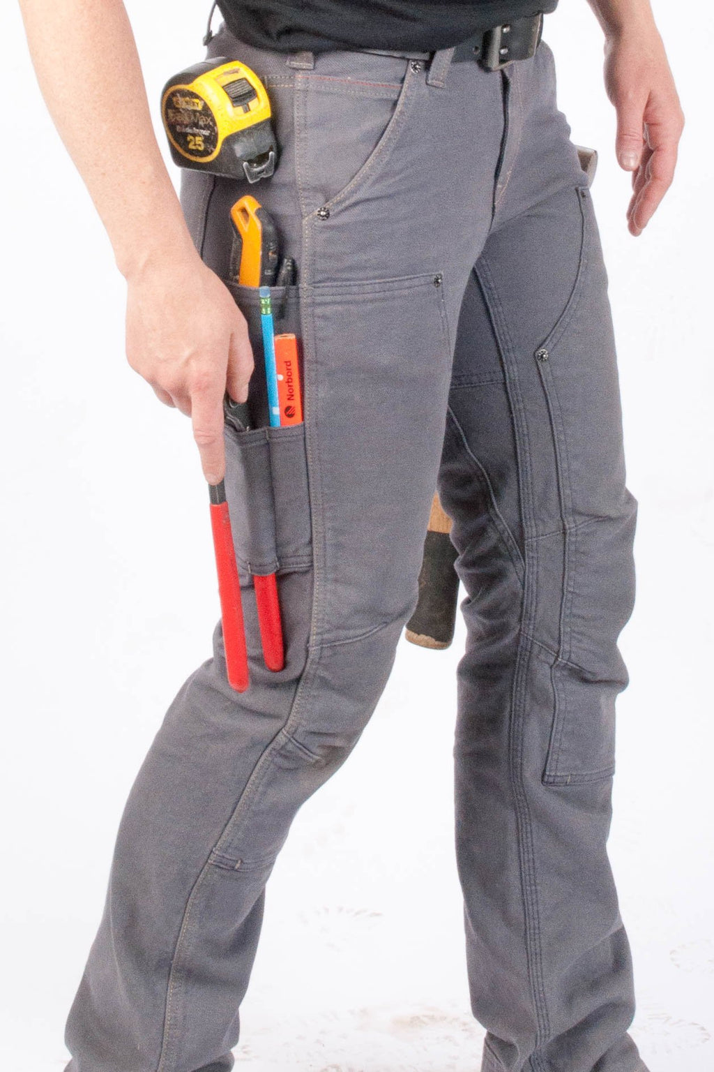 Lower half of Britt Smyton,  the namesake of the Britt Utility pant she is wearing. The Britt Utility Workpant for Women in Grey Stretch Canvas has a measuring tape, penci, plyers, hammer, and multiple tools in her side pockets on the right. On the left, the handle of a has a hammer can be seen popping out from The Britt Utility's modified hammer loop. 