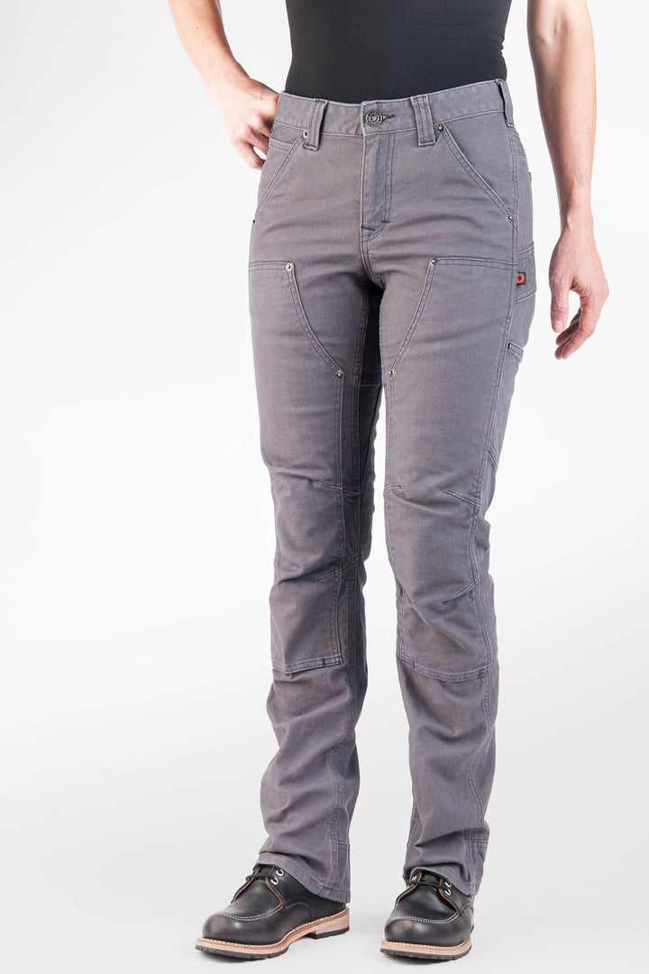 Front of the Britt Utility workpant for women in grey stretch canvas. Kate Day has her left hand on her hip, and her right hand on her side. The front of the pant shows the looser straight leg fit of the Britt Utilty, as well as its reticulated, open knee panels that can fit a kneepad. She is wearing black workboots and a black tanktop. 